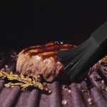 Delicious juicy meat steak cooking on grill. Prime rare roast grilling beef. Electric roaster, rosemary black pepper, salt. Silicone cooking brush.